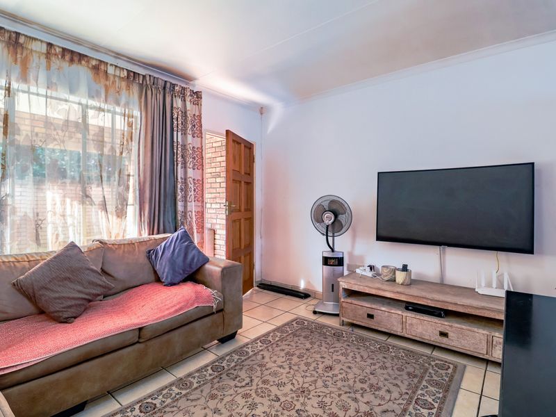 A functional living room featuring tiled flooring, a timber entrance door, and a window fitted with security bars.