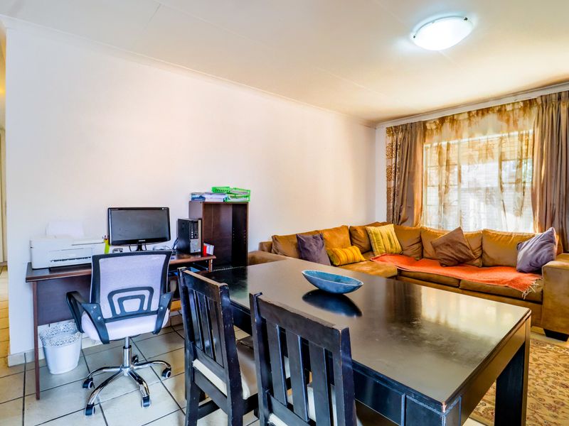 A functional living area featuring neutral tiled flooring and a central ceiling light fixture, providing a versatile space for relaxation and dining.