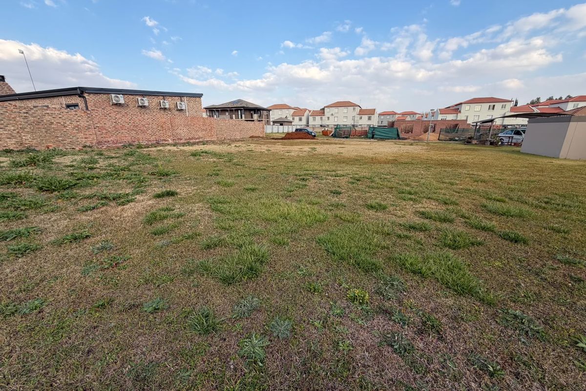 A vacant residential plot featuring a grass lawn and a brick boundary wall, situated in a developed neighborhood.