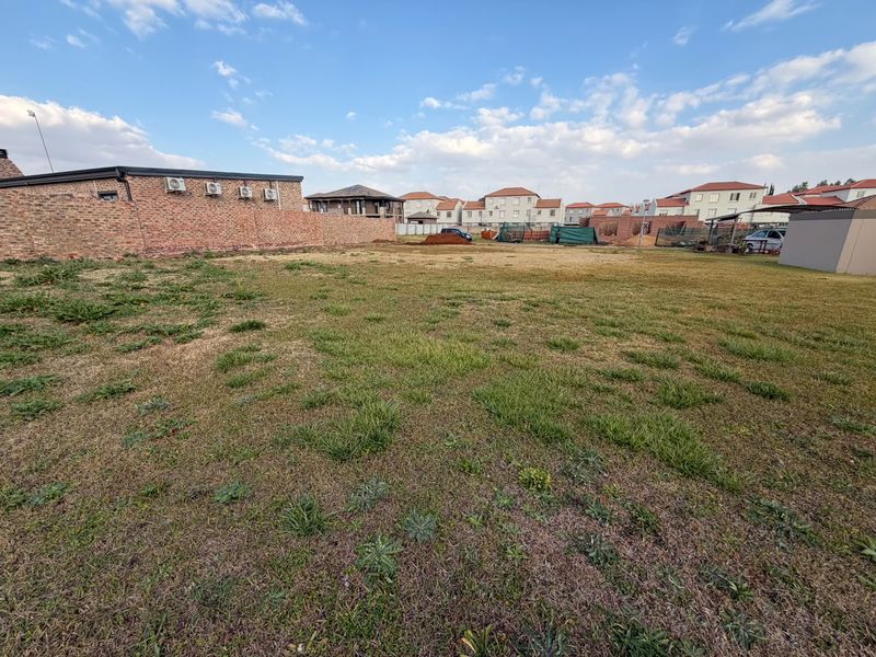 A vacant residential plot featuring a grass lawn and a brick boundary wall, situated in a developed neighborhood.