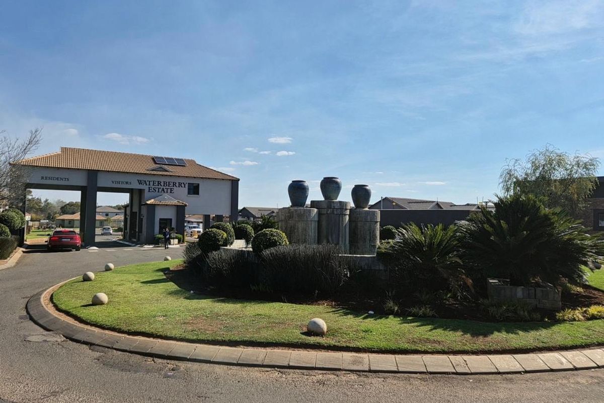 The main entrance to Waterberry Estate, featuring a secure gated access point, a landscaped roundabout with a water feature, and paved driveway infrastructure.