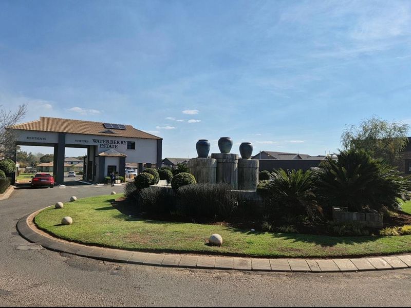 The main entrance to Waterberry Estate, featuring a secure gated access point, a landscaped roundabout with a water feature, and paved driveway infrastructure.