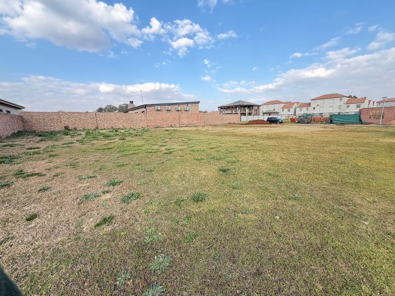 A spacious, level vacant residential plot enclosed by a brick perimeter wall, offering a clear area ready for development.
