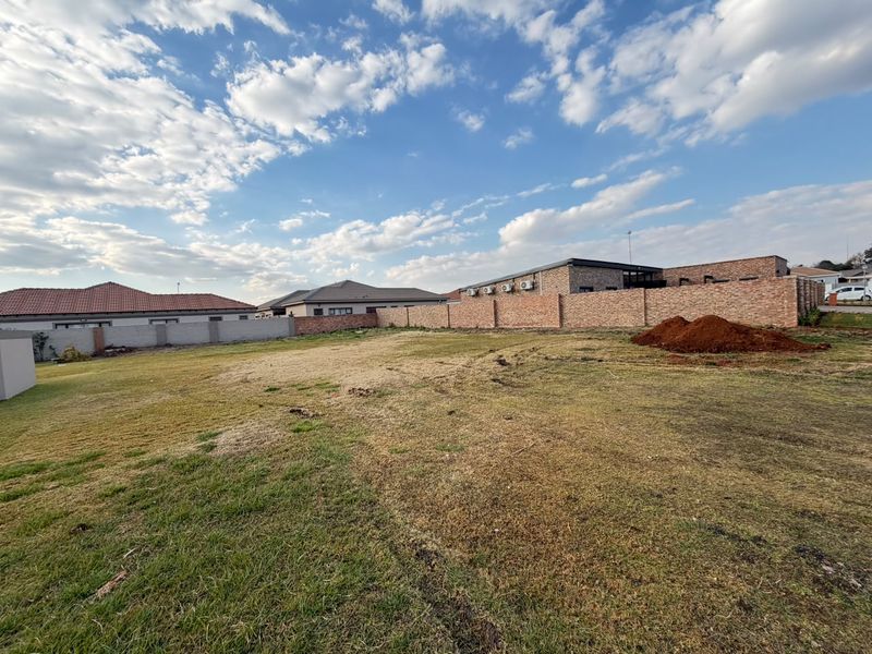 A vacant residential plot featuring a grass lawn and enclosed by a brick boundary wall.