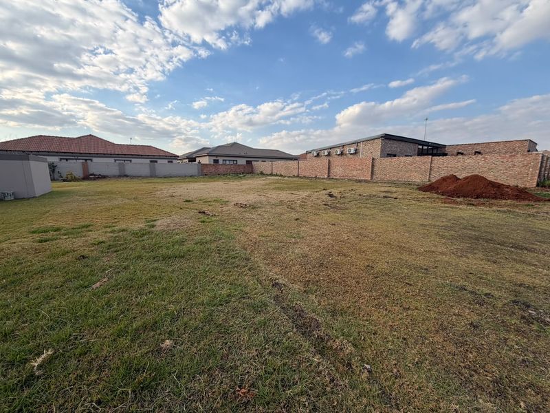 A spacious, level residential plot featuring a well-defined perimeter brick wall and established grass lawn, ready for development.