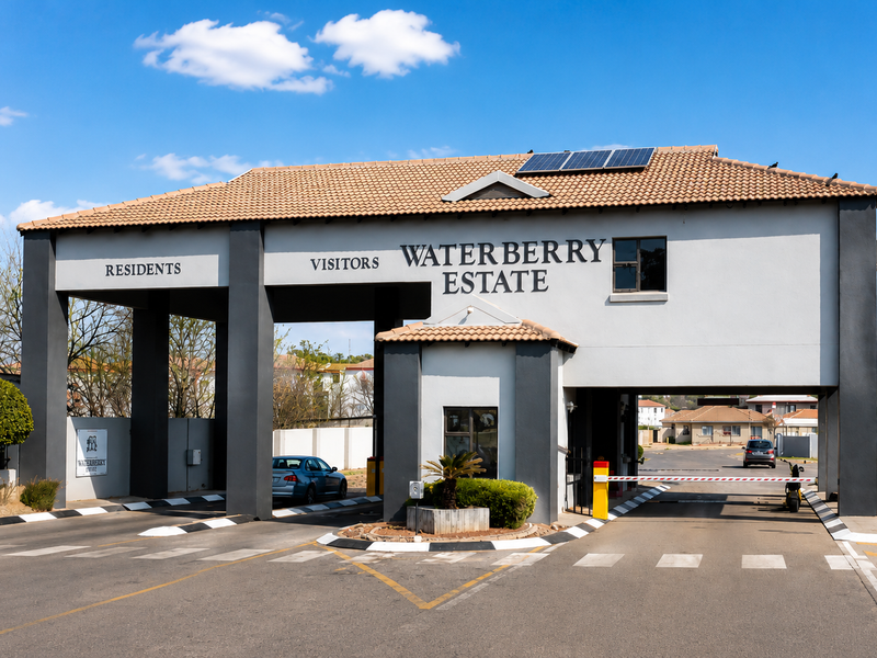 The main entrance gatehouse of Waterberry Estate, featuring a secure access point, boom gates, and solar panels on the tiled roof.