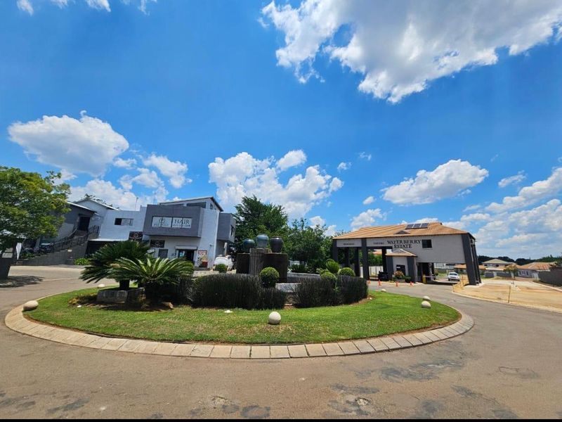 The entrance to Waterberry Estate featuring a landscaped roundabout with a central water fountain and a modern security gatehouse.