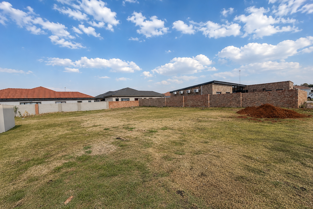 A vacant residential plot featuring a grass lawn and perimeter brick walling, situated in a developed neighborhood.