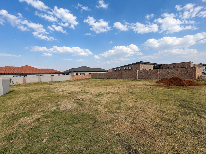 A vacant residential plot featuring a grass lawn and perimeter brick walling, situated in a developed neighborhood.