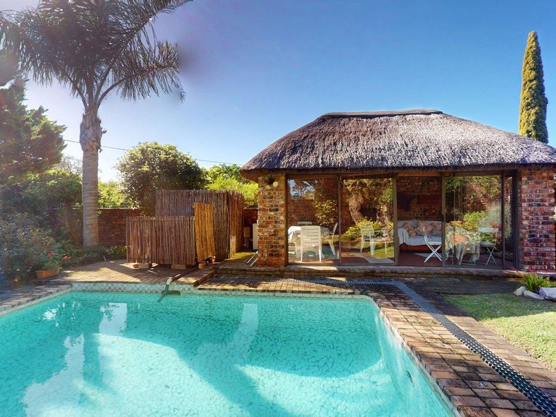 Outdoor pool area featuring a brick-built lapa with a thatched roof, sliding glass doors, and surrounding garden space.