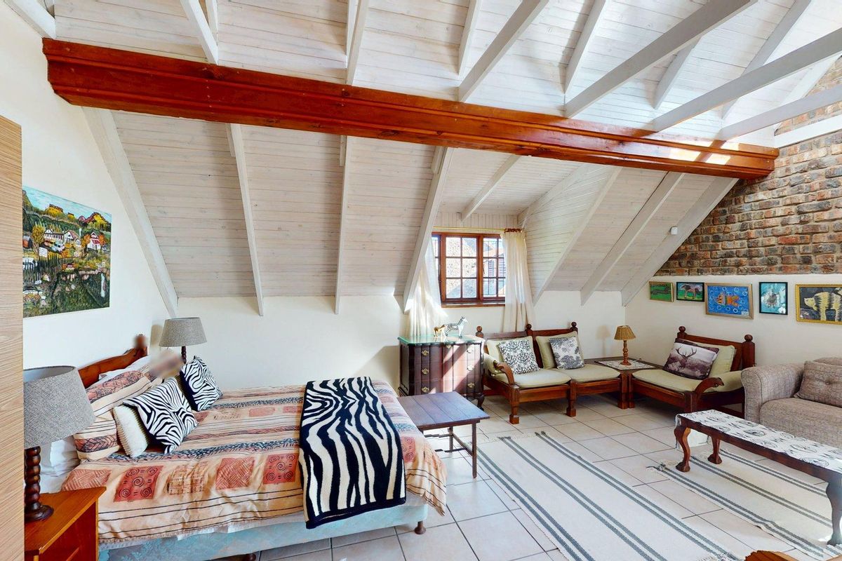 Spacious bedroom featuring a vaulted timber ceiling with exposed beams, tiled flooring, and a rustic exposed brick feature wall.
