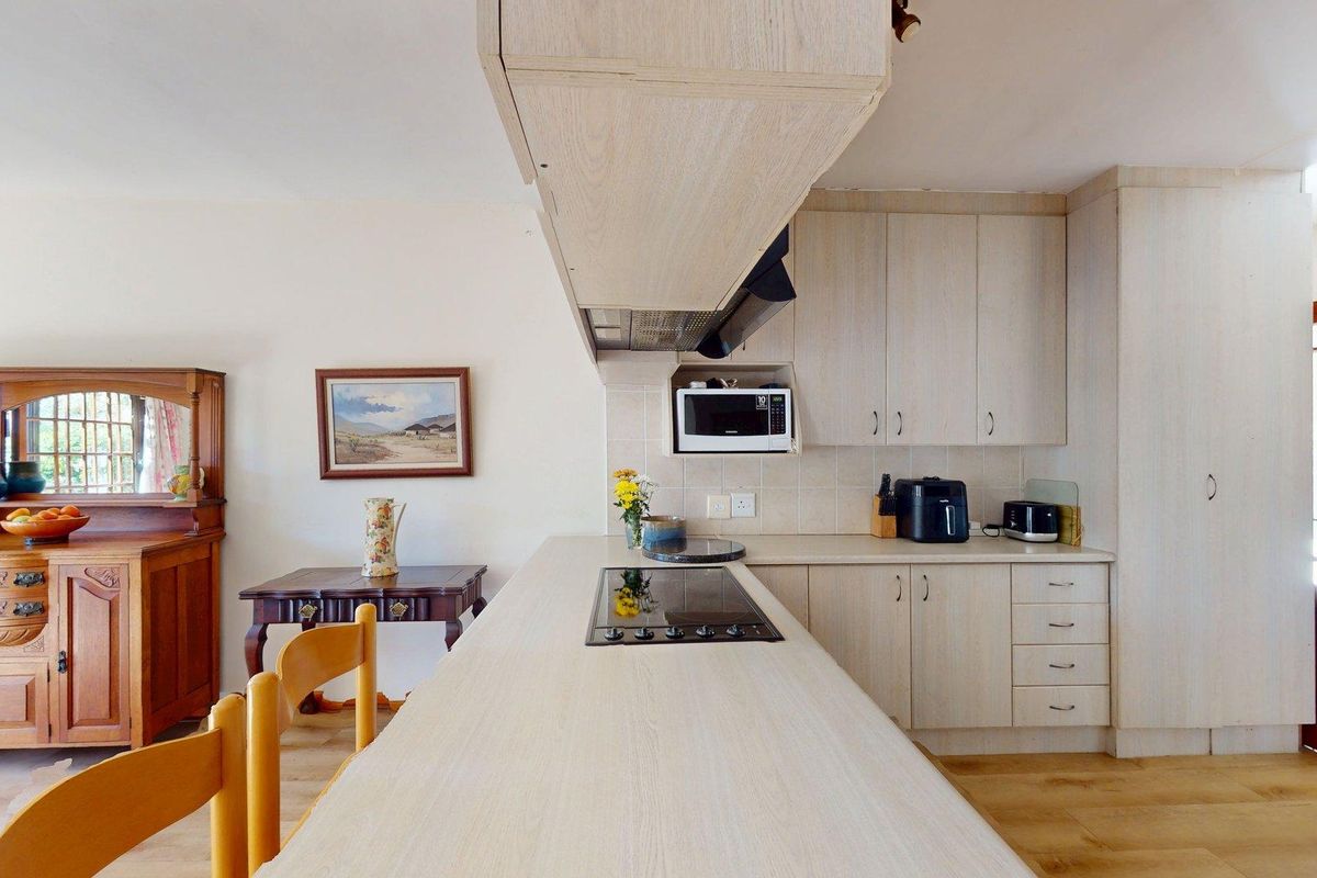 A functional kitchen featuring light wood-look cabinetry, laminate countertops, an integrated hob with extractor fan, and a tiled backsplash.