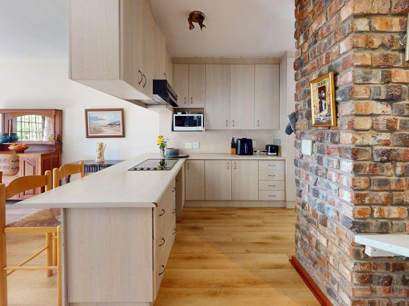 Open-plan kitchen featuring light wood cabinetry, laminate flooring, and a prominent exposed brick feature wall, seamlessly connecting to the dining area.