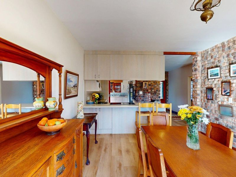Open-plan dining and kitchen area featuring a rustic exposed brick wall, laminate flooring, and functional built-in cabinetry with a breakfast counter.