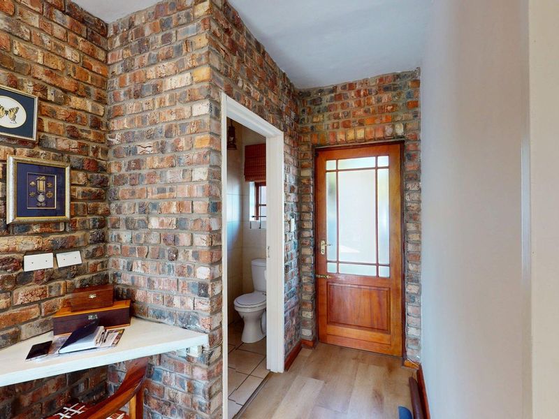 Hallway featuring exposed brick walls, a timber entrance door with glass panels, and a built-in desk area, leading to a small bathroom.