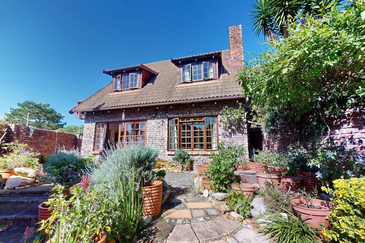 A charming rear exterior view of a brick townhouse featuring a tiled roof, dormer windows, a brick chimney, and a stone-paved patio area.