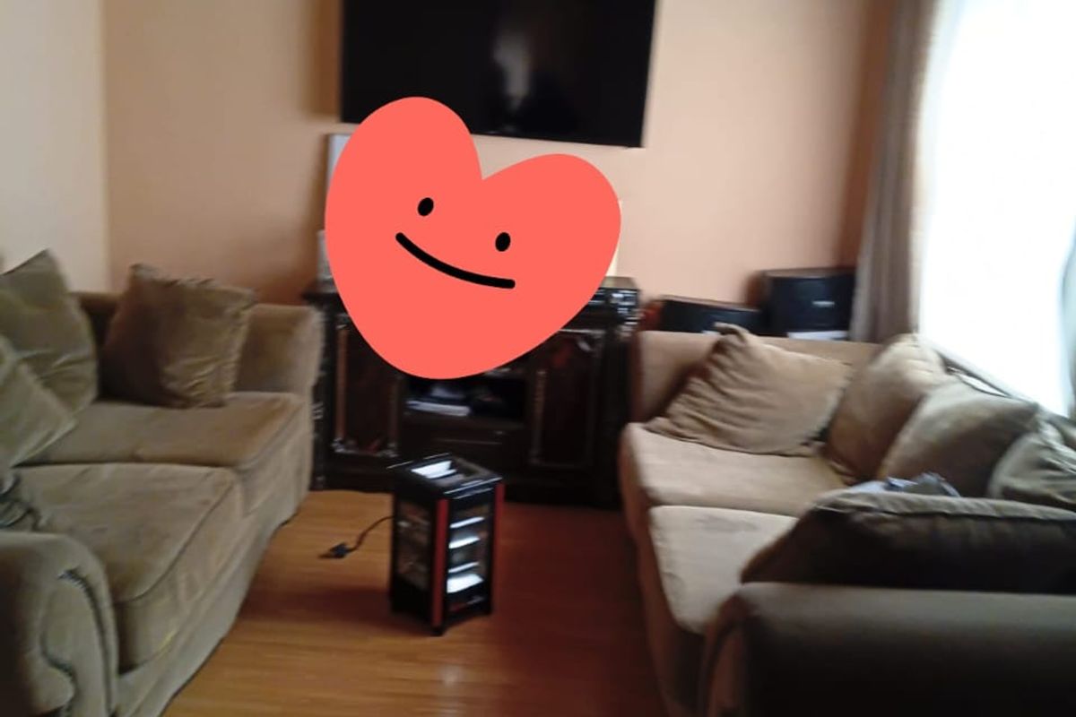 A living room featuring timber ceiling paneling and laminate flooring, currently furnished with seating.