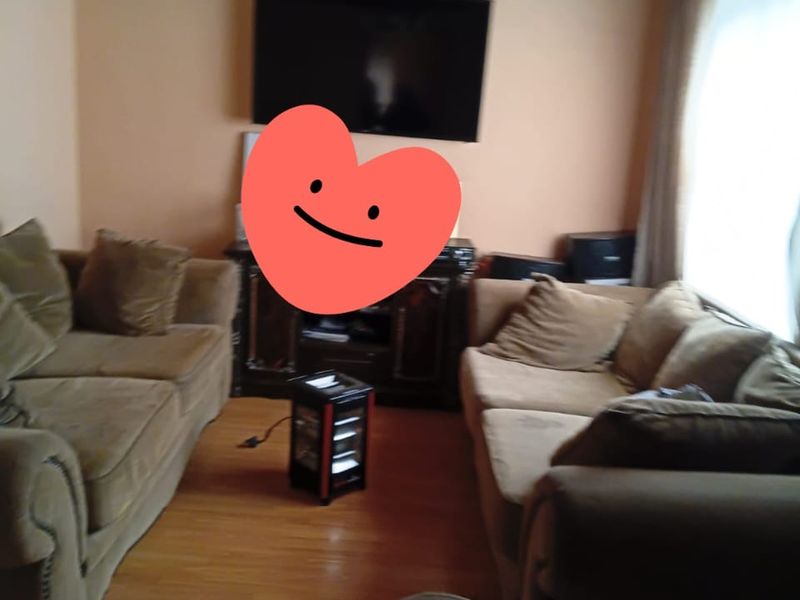 A living room featuring timber ceiling paneling and laminate flooring, currently furnished with seating.