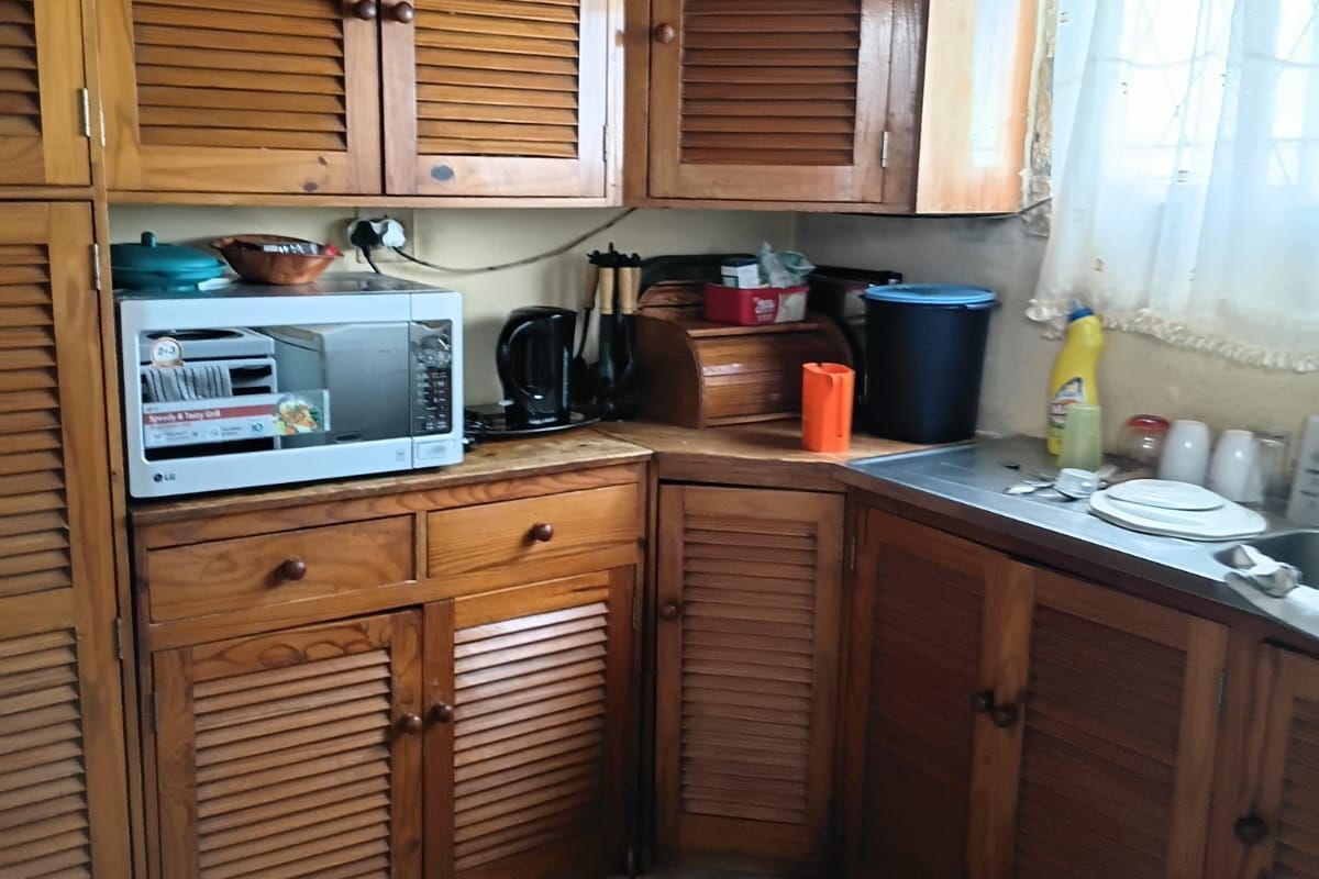 A dated kitchen featuring wooden louvered cabinetry, a stainless steel sink, and tiled flooring in need of repair.