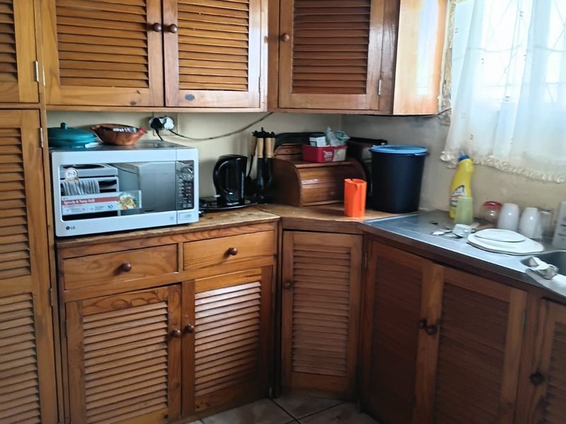 A dated kitchen featuring wooden louvered cabinetry, a stainless steel sink, and tiled flooring in need of repair.
