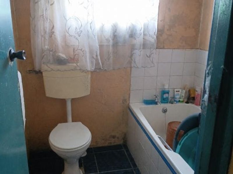 A compact bathroom featuring a bathtub and toilet, requiring significant cosmetic updates to the wall finishes and overall decor.