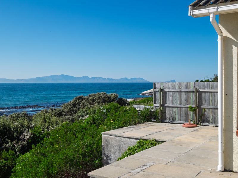 A scenic coastal view from a paved patio area featuring a timber boundary fence and direct ocean outlook.