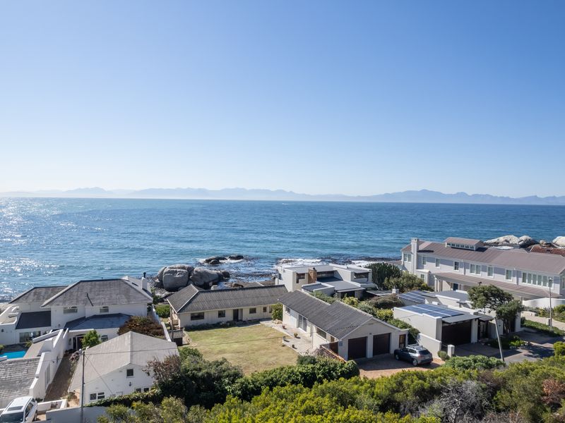 An elevated aerial view of a coastal residential neighborhood featuring homes with tiled roofs, solar panels, and direct ocean views.