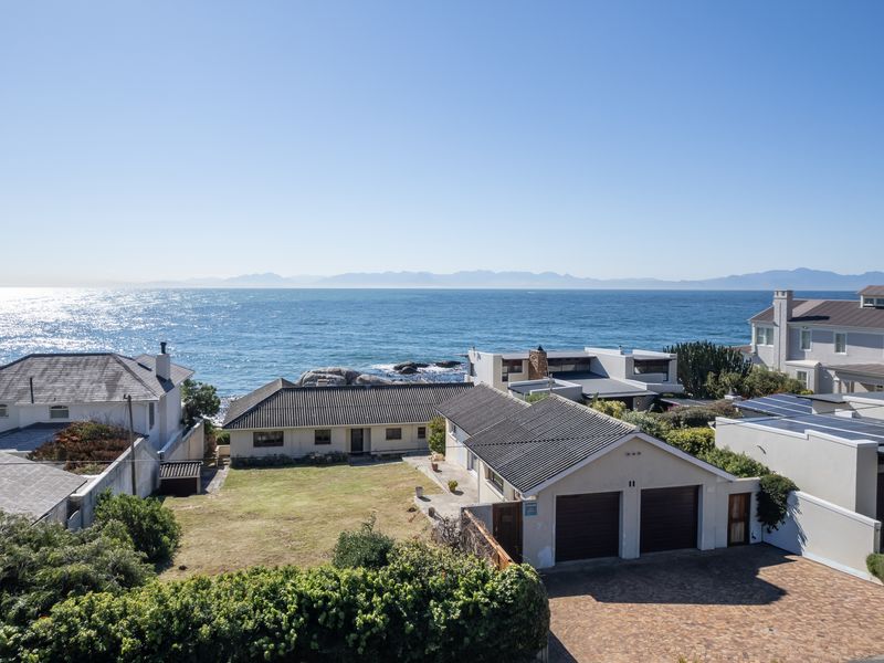 Aerial view of a coastal property featuring a double garage, paved driveway, and expansive ocean views with mountain backdrops.