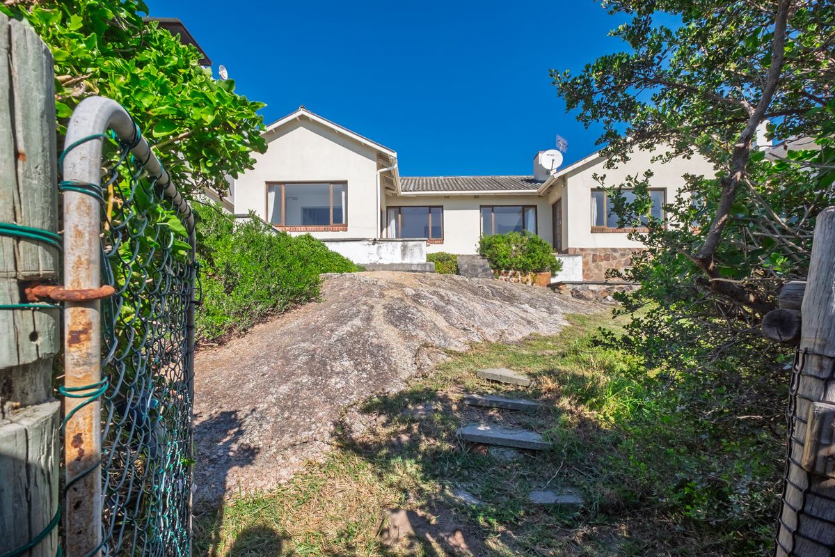 Rear view of the house featuring a natural rock formation in the garden, stone cladding accents, and a tiled roof.