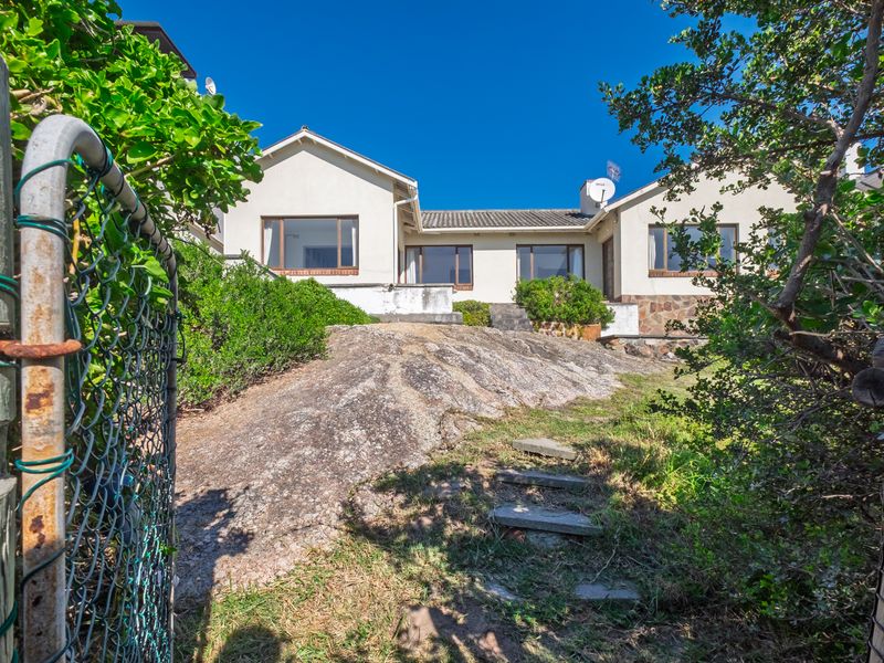 Rear view of the house featuring a natural rock formation in the garden, stone cladding accents, and a tiled roof.