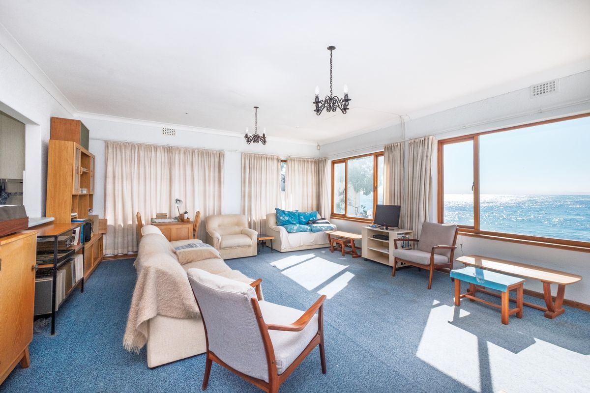 Spacious living room featuring large windows with ocean views, built-in shelving, and classic chandelier lighting, offering a bright and airy atmosphere.