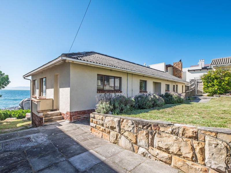 Rear exterior view of the property featuring a stone retaining wall, paved patio area, and direct access to the coastal garden.