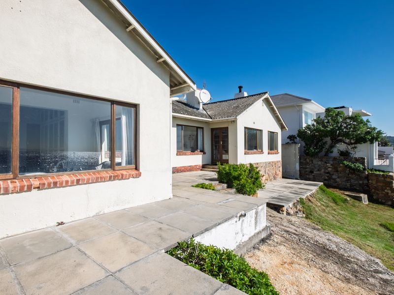 Rear view of the house featuring a paved patio area, brick foundation detailing, and a tiled roof, set against a clear blue sky.