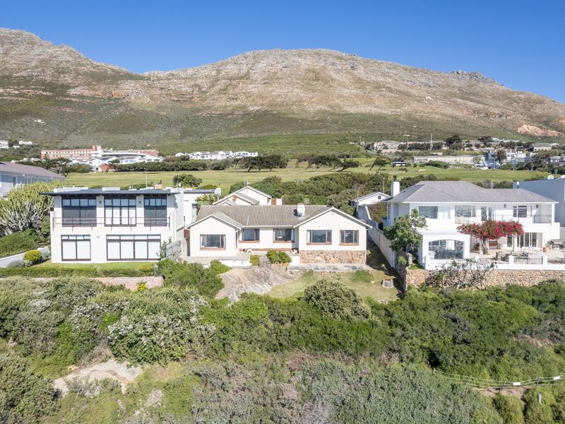 Aerial view of a residential property featuring a tiled roof, stone facade accents, and a rear patio overlooking a coastal landscape.