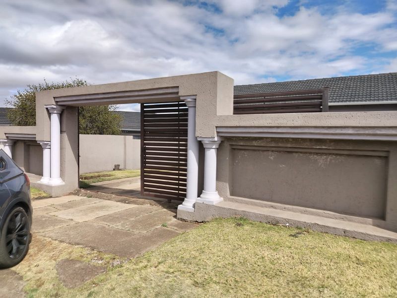 Front entrance view featuring a decorative boundary wall with integrated sliding gate and paved driveway access.