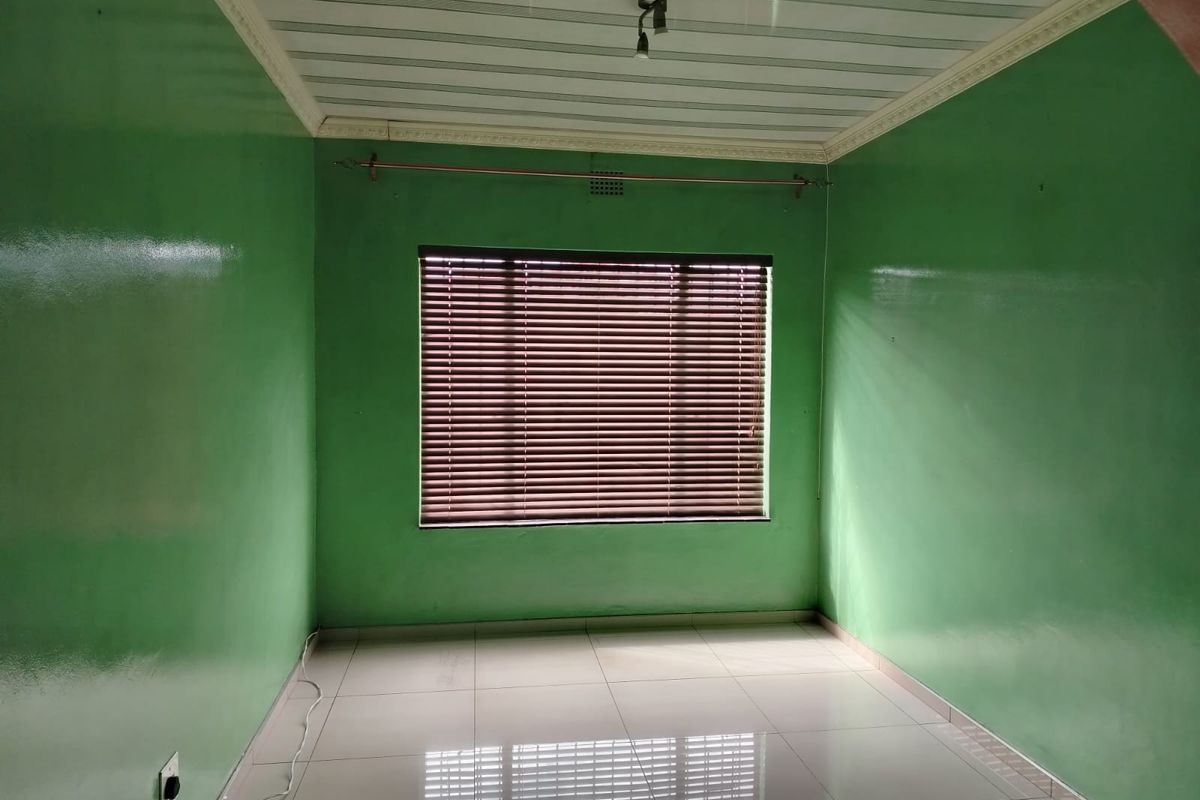 An empty bedroom featuring tiled flooring, a panelled ceiling with cornice detailing, and fitted venetian blinds on the window.