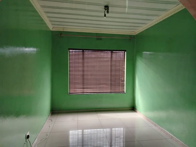 An empty bedroom featuring tiled flooring, a panelled ceiling with cornice detailing, and fitted venetian blinds on the window.