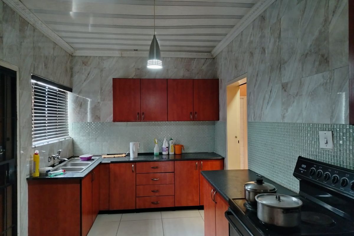 A functional kitchen featuring wood-tone cabinetry, dark countertops, a double basin sink, and a freestanding stove with tiled wall finishes.