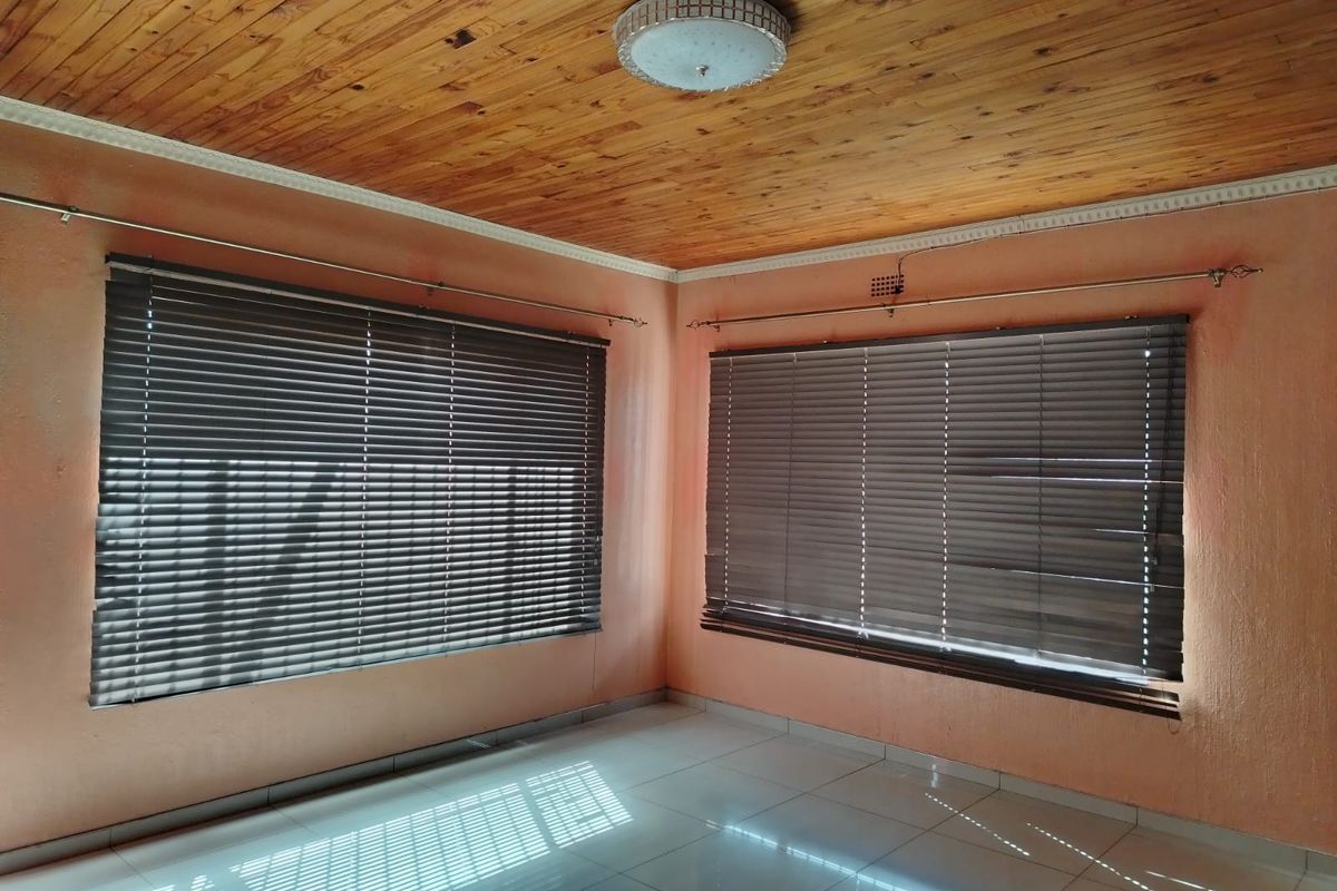 An empty living room featuring a wooden tongue and groove ceiling, tiled flooring, and venetian blinds on the windows.