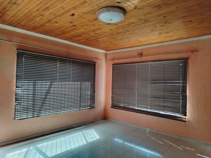 An empty living room featuring a wooden tongue and groove ceiling, tiled flooring, and venetian blinds on the windows.