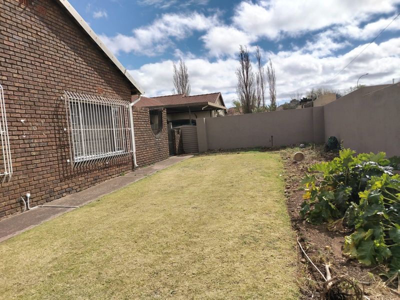 A rear exterior view of the property featuring a brick facade with security bars, a lawn area, and a boundary wall.