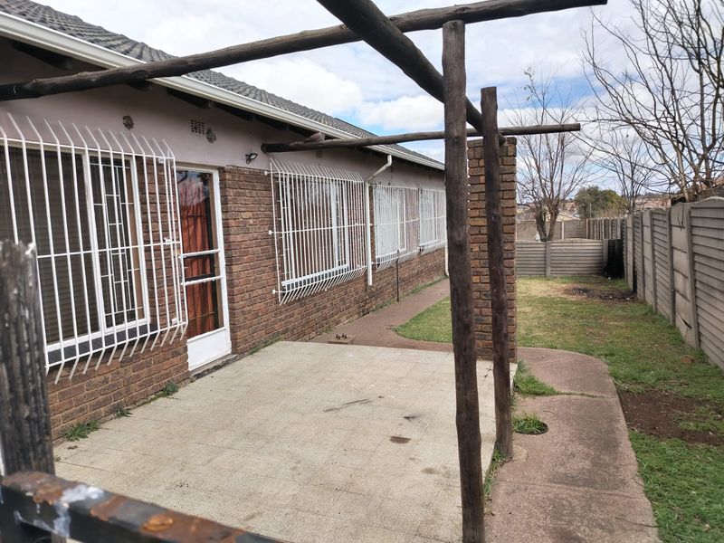 Rear exterior view featuring a brick facade, concrete patio area, timber pergola structure, and a fenced garden with a concrete pathway.