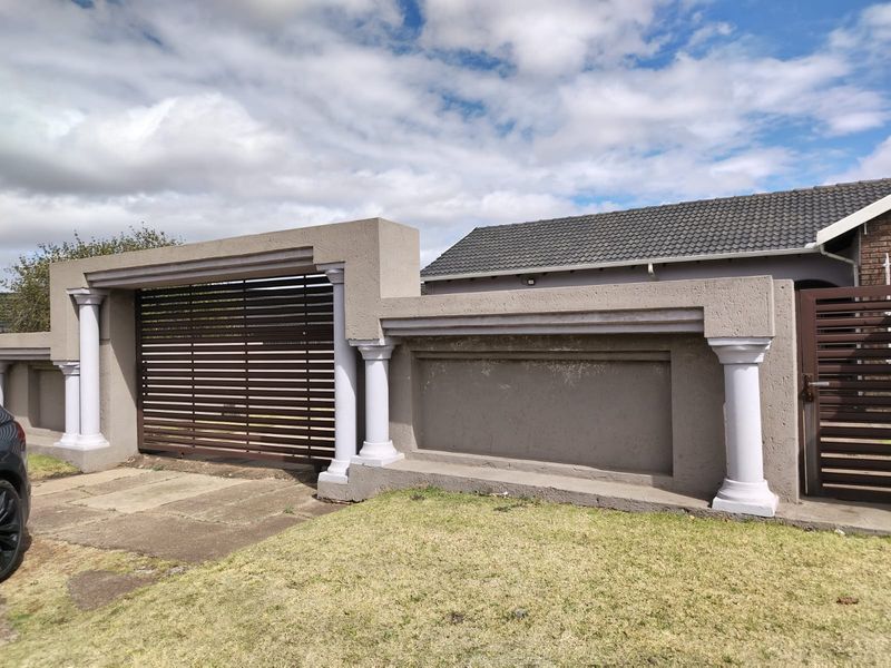Front view of the property featuring a secure boundary wall with integrated sliding and pedestrian gates, decorative columns, and a tiled roof.
