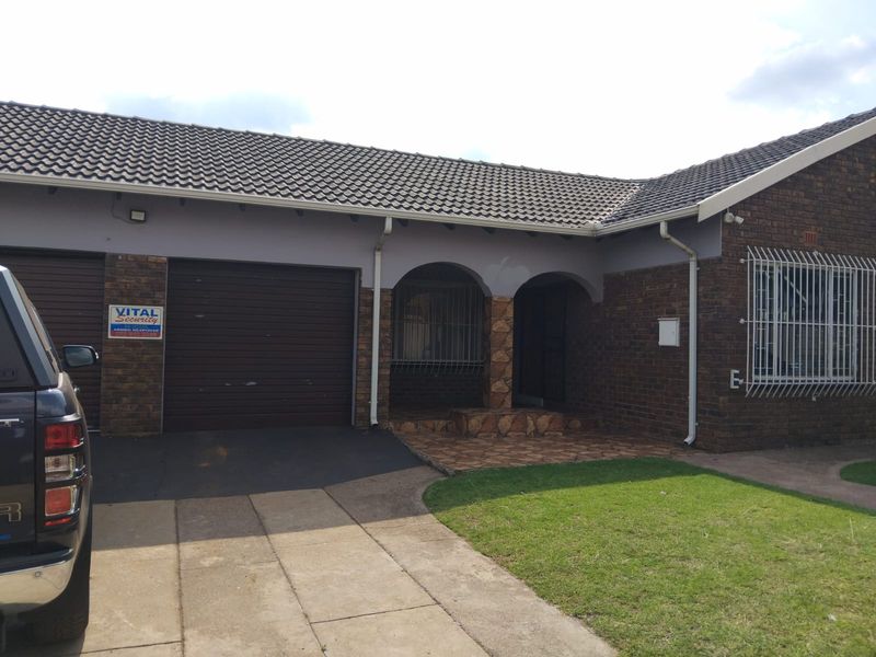 Front exterior view of a brick house featuring a tiled roof, paved driveway, garage, and covered entrance with security bars.