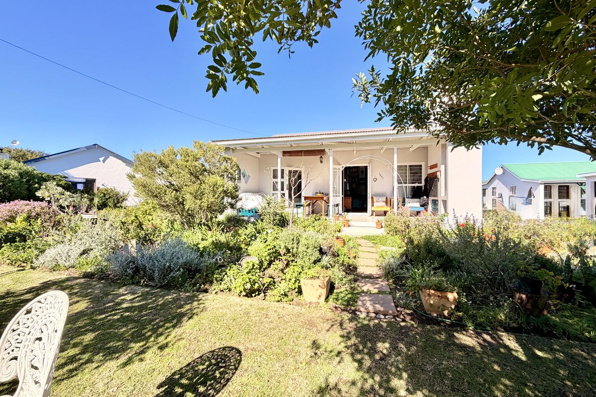A charming rear exterior view featuring a covered patio area overlooking a lush, well-established garden with a stone pathway.