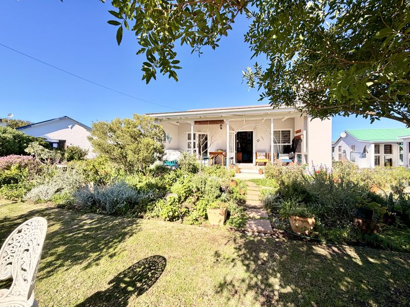 A charming rear exterior view featuring a covered patio area overlooking a lush, well-established garden with a stone pathway.