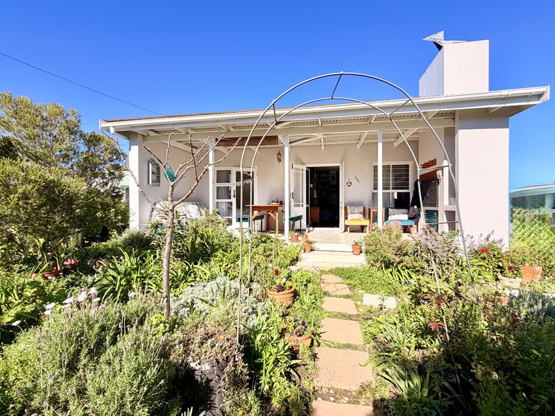 A charming rear exterior view featuring a covered patio, paved garden path, established landscaping, and an external fireplace chimney.