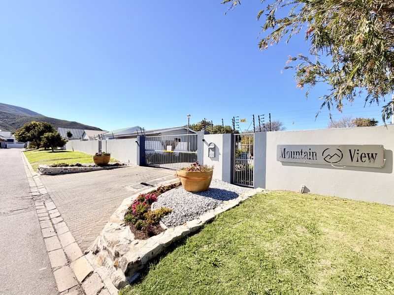 Front entrance view of Mountain View estate featuring a paved driveway, secure metal gate, boundary wall with electric fencing, and landscaped stone garden beds.