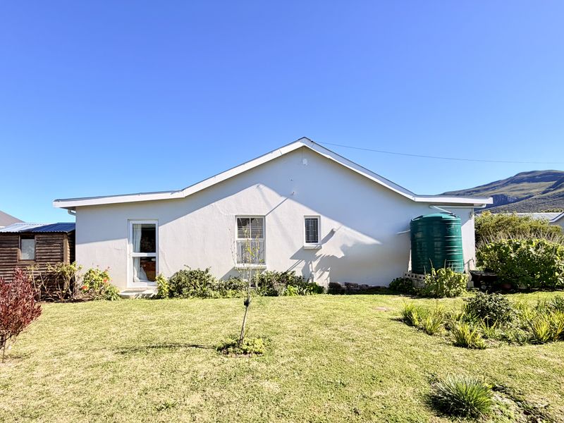 Rear view of the property featuring a well-maintained lawn, landscaped garden, a timber storage shed, and an external water tank.