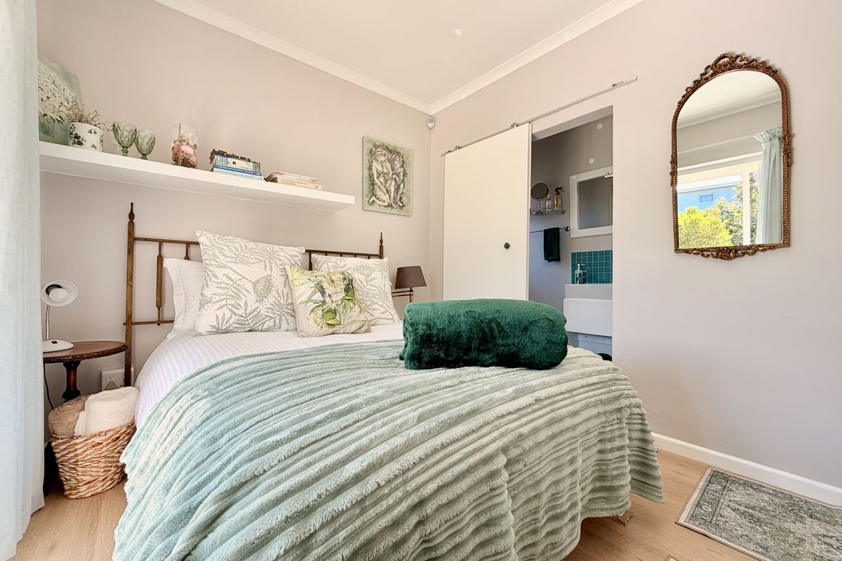 A well-maintained bedroom featuring light laminate flooring, a floating shelf, and a sliding door providing access to an adjoining bathroom.